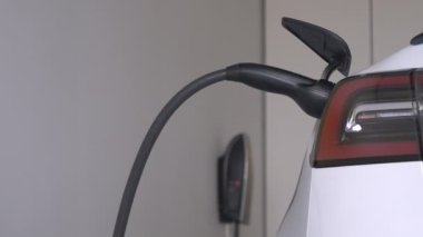 Ev garajındaki şarj istasyonuna takılı beyaz elektrikli araba. Siyah güç kablosu motorun bataryasını çalıştırmak için BEV 'e bağlı. Modern ulaşım için sıfır emisyon alternatifi.