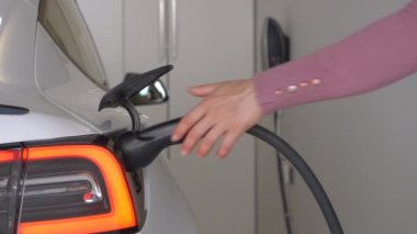 Kimliği belirsiz bir kadın elektrikli bir arabayı şarj istasyonundan ayırdı. Kadın sürücü bir BEV 'den siyah elektrik kablosu çıkarmış. Alternatif ve yeşil ulaşım araçları için zahmetsiz bir sistem.