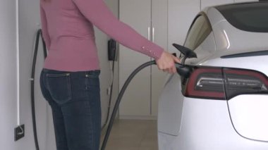 Kadın elektrikli bir arabaya yaklaşır ve onu garajdaki şarj ünitesinden ayırır. Genç bayan beyaz elektrikli bir araca biniyor ve tam dolu bir akü ile gitmeye hazır.