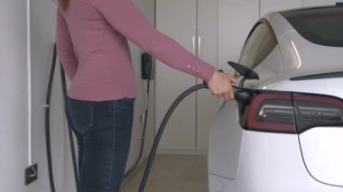 Kadın fişini çekti ve garajdan çıkmak için elektrikli arabaya bindi. Kadın sürücü bir BEV 'den siyah elektrik kablosu çıkarmış. Alternatif ve yeşil ulaşım araçları için zahmetsiz bir sistem.