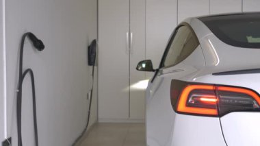 Garaja park ettikten sonra, bir kadın şarj için elektrikli bir araba takıyor. Genç bayan sürücü, araba kullandıktan sonra motorun pilini şarj etmek için siyah elektrik kablosunu beyaz elektrikli aracına bağlıyor..