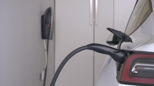 在家用车库连接零排放Bev充电发动机电池 白色电动汽车用电线插入充电站 现代运输的有效替代办法 — 图库视频影像