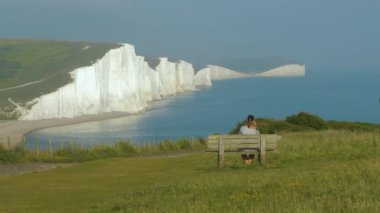 Gezgin ahşap bankta oturuyor ve güzel beyaz uçurumların fotoğraflarını çekiyor. Genç kadın Güney İngiltere 'de geziyor ve resimli kıyıları keşfediyor. Muhteşem manzaralı Vantage Noktası.