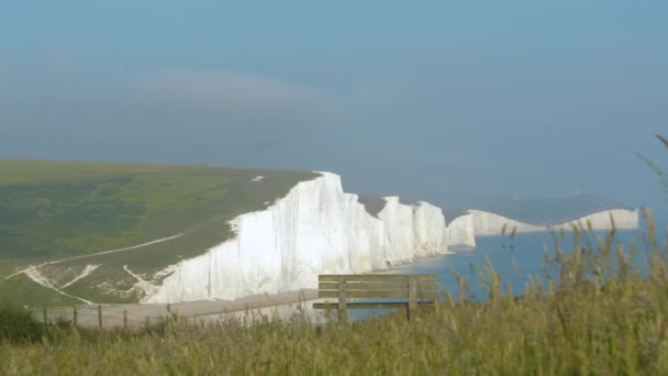 海の上に上昇する息をのむような白い崖の素晴らしい眺めの木製のベンチ 南イングランドの海岸に沿って伸びる美しいチョーク崖でリラックスして賞賛する場所 — ストック動画