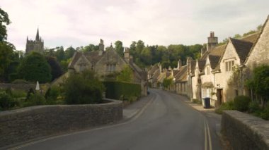 Tatlı taş evlerle dolu bir köy masalına giriyoruz. Yeşil bir tepenin altındaki sarmal asfalt yol boyunca çok güzel bir Castle Combe 'da manzaralı teraslı kulübeler.