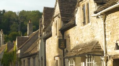 COTSWOLDS, WILTSHIRE, UNITED KINGDOM, 15 Eylül 2023: GERÇEK: Güzel cepheler ve taştan yapılmış eski evlerin çatıları. Yeşil tepenin altında teraslı kulübeleri olan görkemli bir köy..