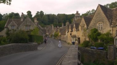 COTSWOLDS, WILTSHIRE, UNITED KINGDOM, 15 Eylül 2023: Eski taş evlerle birlikte pitoresk köylerde gezinen turist ziyaretçileri. Sıcak yaz günlerinde kırsal köyleri gezmek