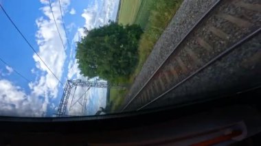 POV VERTICAL: Güneşli bir günde manzaralı İngiliz kırsalında demiryolu yolculuğu. Pencereden dışarı bakan tren tarımsal tarlalardan ve gözün görebildiği kadar uzağa uzanan yeşil çayırlardan geçiyor..