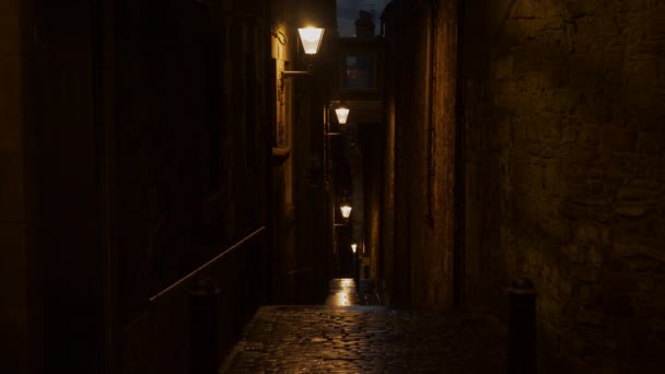 街灯点亮的中世纪城镇的一条黑暗而狭窄的小巷 山下鹅卵石铺成的小街 周围是被夜晚街灯照亮的旧城房屋的石墙 — 图库视频影像