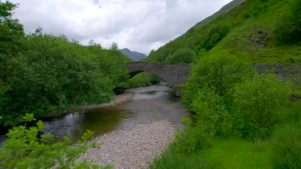 エリアル 緑豊かな山の間の緑と牧草地の間に流れるシール川の上の魅力的な石橋 過去に触れたスコットランドの高地の風景 — ストック動画