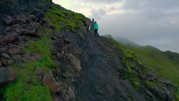 エリアル 女性は素晴らしい大聖堂ロックの景色が開いたときに急な道を登ります 若い旅行者はスコットランドのスカイ島の嵐で驚くほど美しい自然のアトラクションを探索します — ストック動画