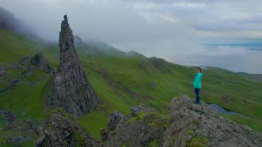 Kadın Storr 'un İhtiyar Adamı' na doğru yürürken nefes kesici manzaraya hayran. Genç turist, Skye Adası 'ndaki Katedral Kayası' nın üzerinde duran eşsiz manzaradan etkilendi..