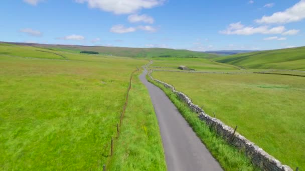 ウインディングロードは 石の壁に囲まれた鮮やかな緑色の過去をリードします 草の牧草地の真ん中にある伝統的な畑の納屋 美しい晴れた夏の日のイギリスの田舎の写真 — ストック動画