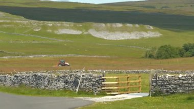 Traktör, güzel, güneşli bir yaz gününde İngiltere 'nin manzaralı kırsalında kuru taş duvarlı bir çayırda çim biçer. Yorkshire Dales Ulusal Parkı 'nın cennet yeşili kırsalında modern tarım.