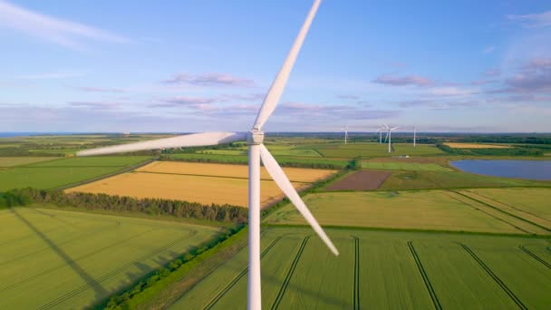 イギリスの田舎の風力発電所で風力タービンを回転させます 美しい農地の上の風車の白い刃を紡いでいる 風を利用して電気エネルギーを発生させる — ストック動画