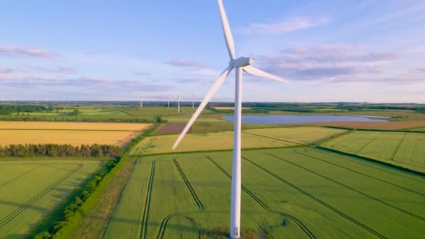 エリアル Close 農村部の風力発電所で白い風車ブレードを紡ぎました 美しい風景のフィールドの上に上昇する背の高い近代的な発電の構造を持つ英国の田園地帯 — ストック動画