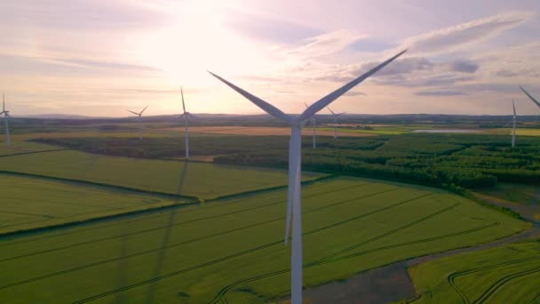 エリアル レンズフリー 農地と回転風車の上にカラフルな日没の空 美しい風景のフィールドの上に上昇する背の高い近代的な発電の構造を持つ英国の田園地帯 — ストック動画