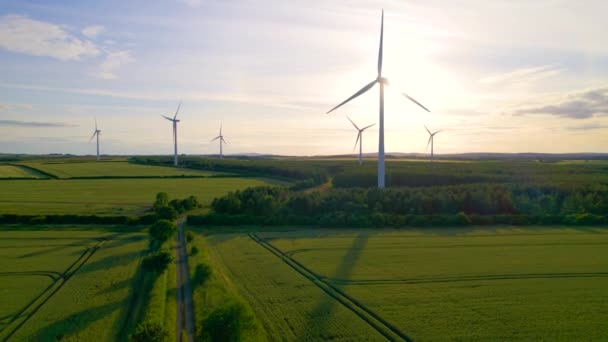 Aerial Lens Flare 黄金の朝の日光は 美しい緑のイギリスの田舎の風力発電所で風力タービンを回転させることによって輝きます 高い現代風力発電された構造は電気を発生させます — ストック動画