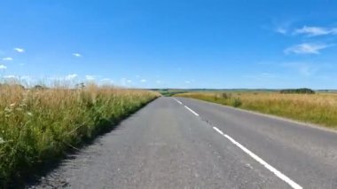Güzel İngiliz kırsalında asfalt bir yolda arabayla seyahat etmek. Sol elle yeşil tarlaları ve otlakları geçerek güneşli bir yaz gününde resimli yuvarlanan araziye yayılıyor..