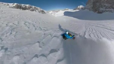 Tanınmaz haldeki snowboardcu taze kar tanesi üzerinde bir dağdan aşağı iniyor. Alplerde güzel güneşli bir günde korkusuz genç adam dik yamaçlarda uçarken beyaz toz kar etrafta uçuşuyor..