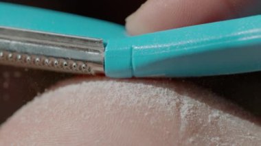 Keskin ayak dosyası, genç bir kadının topuğunun kabarık nasırlı derisini kaldırır. Özel bir pedikür dosyasıyla kuru derinin alındığını gösteren ayak derisinin yakın plan görüntüsü..