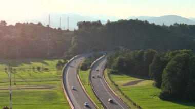 Yaz otobanı trafiğinin tünele giriş çıkışının insansız hava aracı videosu. Çevre yolu yaz erken bir günde meşguldür. Arabalar yeşil tarlaların ve ağaçların yanından geçiyor..