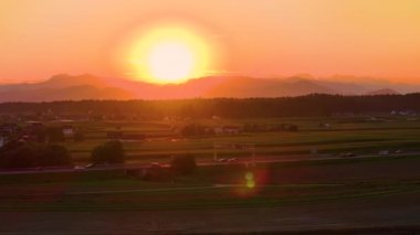 AERİAL, LENS FlaRE: kırsal otoyolda sürüş sayısız araba üzerinde altın saat akşam güneş ışınları parıldıyor. Gün batımı huzurlu kırsal kesimi aydınlatırken, banliyö sakinleri manzaralı otoyol boyunca araba kullanıyorlar..