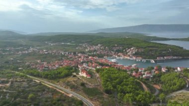 Yeşilliğin üzerinden uçarak Hırvatistan 'ın Hvar adasının manzaralı marinasına doğru. Adriyatik 'teki ünlü bir turist adasının yamacına yayılmış bir sahil kasabasının manzarası.