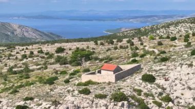 Güneşli bir Akdeniz adasının tepesinde taş bir duvarla çevrili küçük bir kilisenin etrafında uçuyor. Hvar adasının uzak bir köşesindeki engebeli arazide küçük bir şapelin manzarası..
