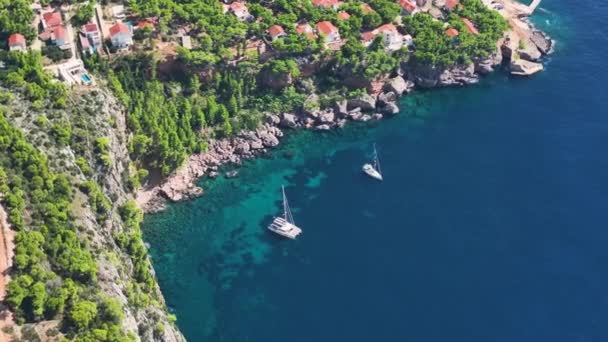 安乐死的游艇停靠在幽静的海湾碧绿的海水中 旁边是陡峭的悬崖和茂密的地中海绿地 飞越两艘停泊在Hvar海岸的帆船 — 图库视频影像