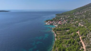 Hırvatistan 'ın Hvar adasının ücra bir köşesinde, Akdeniz kıyısı boyunca ve uykulu bir okyanus kıyısındaki köy boyunca uçuyor. Sahildeki evlerin altında manzaralı bir adada küçük bir körfezin görüntüsü..