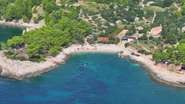 Gözlerden uzak bir Hvar yerleşim yerinin yakınındaki küçük kayalık bir körfezin nefes kesici görüntüsü. Açık mavi sularda kürek çekenlerle güneşli plajın üzerinde uçmak. Küçük bir tepenin üzerine tünemiş birkaç ev var..