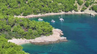 Hvar adasının ücra bir köşesindeki gözlerden uzak bir körfezin manzaralı bir görüntüsü. Birkaç ziyaretçisi olan küçük, gizli bir sahil. Yakınlarda birkaç demirlemiş tekne ve dinlenen insanlar var..