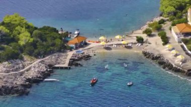 Turistler Hvar adasının kıyılarındaki yaz etkinliklerinin tadını çıkarıyorlar. Turkuaz denize bakan koltuklarıyla kumlu bir plajın üzerinde uçuyorlar. Yazın Dalmaçya 'nın insansız hava aracı görüntüsü.