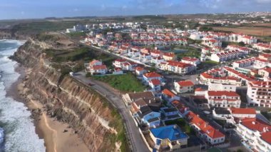Portuguese seaside village with white terraced houses on the edge of a cliff. Small coastal town boasts terracotta rooftops and neat rows of homes that overlook a dramatic cliffside rising above ocean