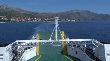 Ferry departure to a Croatian island with a picturesque view of beautiful coast. A ferry boat sails towards the open sea, offering a spectacular view of a coastal town against a mountain backdrop.