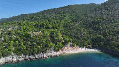 Korcula adasındaki ıssız bir çakıl taşı plajının üzerinde yemyeşil Akdeniz tepeleri yükseliyor. Adriyatik Denizi 'ndeki küçük bir adanın engebeli bitki örtüsünün altında gizlenmiş panoramik drone görüntüsü.