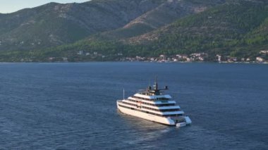 KORCULA ADASI, CROATIA, 5 Mayıs 2024, AERIAL: Güneşli bir yaz akşamında Adriyatik Denizi 'nde yelken açan büyük bir yatın manzarası. Şatafatlı bir yat Korcula 'dan gün batımında açık denizlere açılacak..