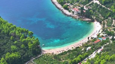 Turistlerin şemsiyeleriyle dolu muhteşem turkuaz sularla manzaralı bir plajın üzerinde uçmak. Güneşli bir yaz gününde Korcula adasında manzaralı bir halk plajı manzarası..