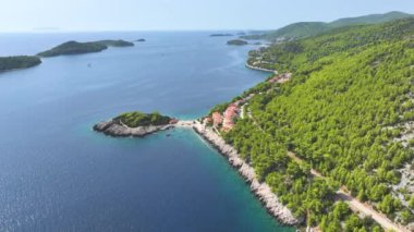 Korcula adasında kristal berrak mavi denizle çevrili küçük bir yarımadayı gösteren panoramik bir kıyı yolu manzarası. Hırvatistan 'ın Dalmaçya kentindeki yeşil Akdeniz adası boyunca uçuyor.