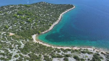 Adriyatik 'in turkuaz sularının Murter' deki uzak bir plajın yakınındaki resimli hava manzarası. Dalmaçya 'nın yemyeşil yeşillikleriyle çevrili tenha kayalık bir sahilin nefes kesici drone görüntüsü..