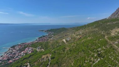 Güneşli bir yaz gününde, kıyı kasabası Omis 'in kırsal kesiminin manzarası. Hırvatistan 'ın Dalmaçya kentindeki Akdeniz kıyısı ve uykulu bir okyanus kıyısındaki köy boyunca uçuyor.