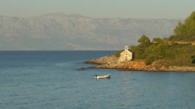 Adriyatik adasının kayalık bir kıyısındaki eski şapel. Dalgalı denizde sallanan çam ormanlarıyla çevrili. Altın gece ışığı, güzel deniz manzarasını aydınlatır. Saklı, huzurlu bir koyda..