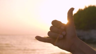 Shaka, altın batan güneşe karşı iyi titreşimler ve aloha ruhu sergileyen el hareketinde bulundu. Güzel bir günbatımının aydınlattığı olumlu bir el hareketi sahilde tatili simgeler.
