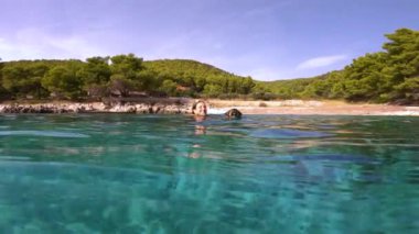 Güneşli Hvar adasında Adriyatik Denizi 'nde köpeğiyle birlikte kameraya doğru yüzen genç bir kadının gülen yüzü. İkisi de ferahlatıcı deniz suyunun tadını çıkarıyorlar..