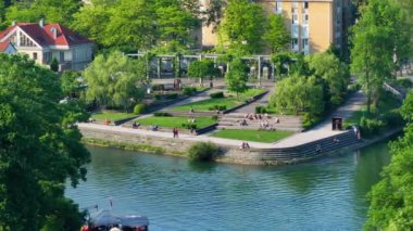 Turistler ve yerliler, güzel zümrüt renkli Ljubljanica nehrinin kenarında güneşin tadını çıkarıyorlar. Tuhaf bir Avrupa şehrinin merkezinde uzanan muhteşem nehrin yanındaki parkın manzarası..