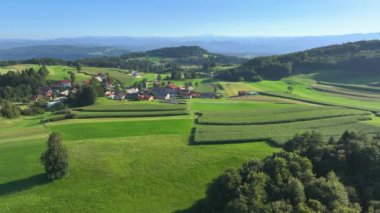 AERIAL: Picturesque little village nestled in the heart of green rolling hills, surrounded by lush fields and forests. Incredible natural beauty and tranquillity of rural setting on a sunny summer day.