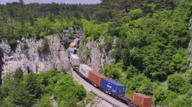 KOPER, SLOVENIA - 2024, 3 Temmuz: Yük treni engebeli, kayalık bir arazide demiryolu boyunca seyahat eder. Çarpıcı doğal manzara ve hareket halindeki bir kargo treniyle inanılmaz şekilde döşenmiş demiryolu hattı.