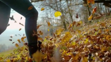 LENS FlaRE, SLOW Motion, KAPALI: Uçan sonbahar yaprakları arasında koşan tanınmayan bir kadın rüzgar estirdi. Güz mevsiminin canlı ve renkli doğasında dışarıda güneşli güzel bir günün tadını çıkarıyor..