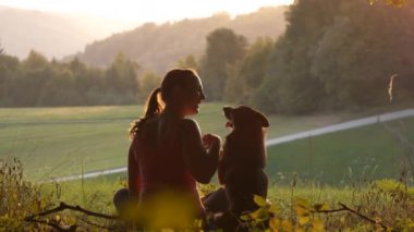 Bir sonbahar manzarasında güzel bir günbatımını izlerken kadının köpeğine sarıldığı dokunaklı bir sahne. Genç bayan, doğada birlikte zaman geçirirken tüylü arkadaşıyla yakın bir bağı paylaşıyor..